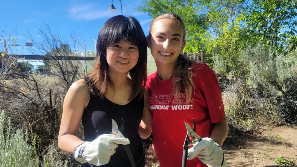 Two honors college students stand, holding pruning sheers while volunteering